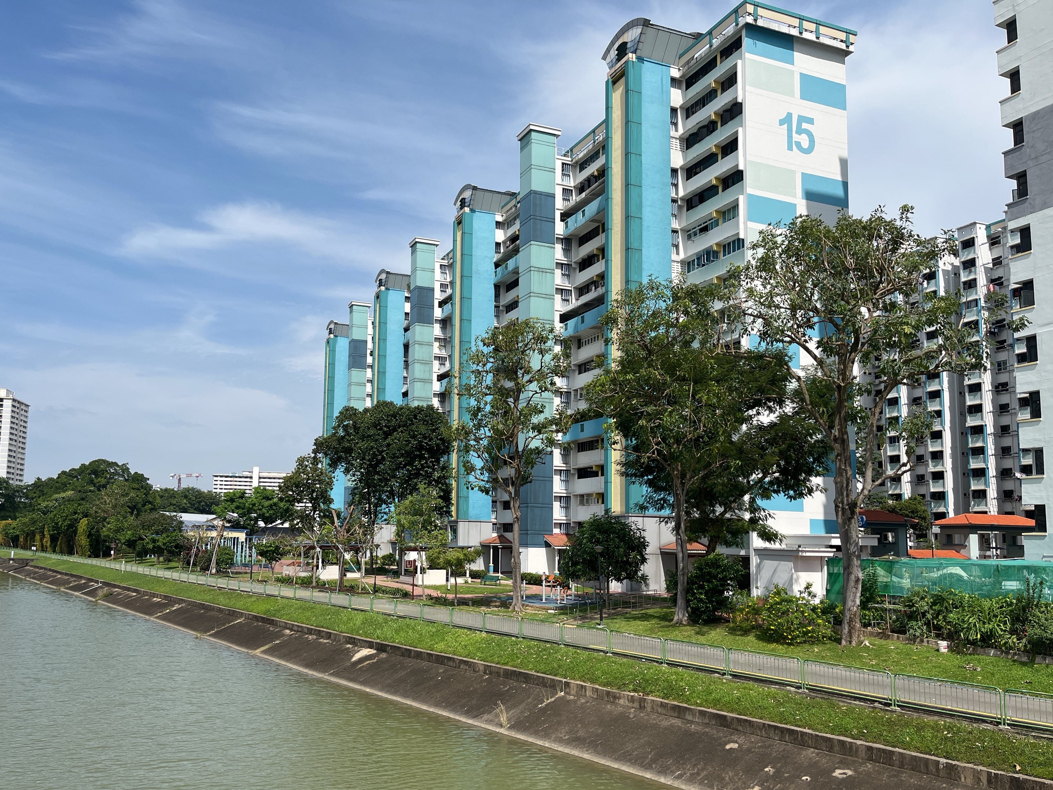 Several tall, blue residential buildings labeled "15" with a canal, path, and trees in the foreground.